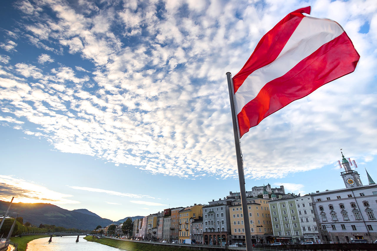 Versand von Laminat, Parkett, Kork und Vinyl nach Österreich Östereich-Flagge weht im Wind mit Blick auf Sazburg